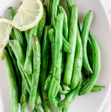 Air fryer green beans on a white plate garnished with a lemon twist.