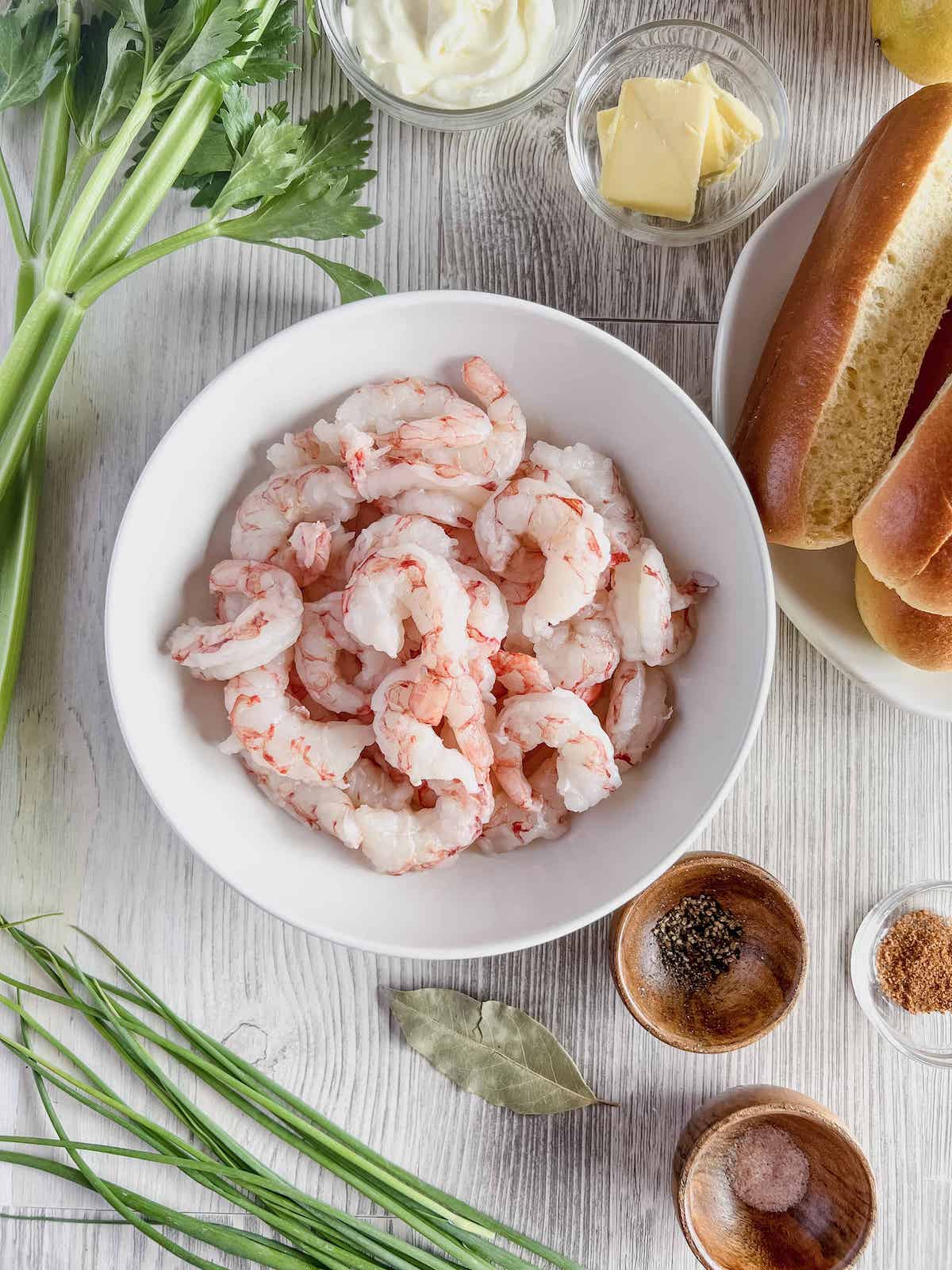 White bowl full of raw argentine red shrimp surrounded by recipe ingredients.