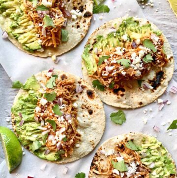 Chicken tinga tacos open flat on a sheet pan lined with parchment paper.