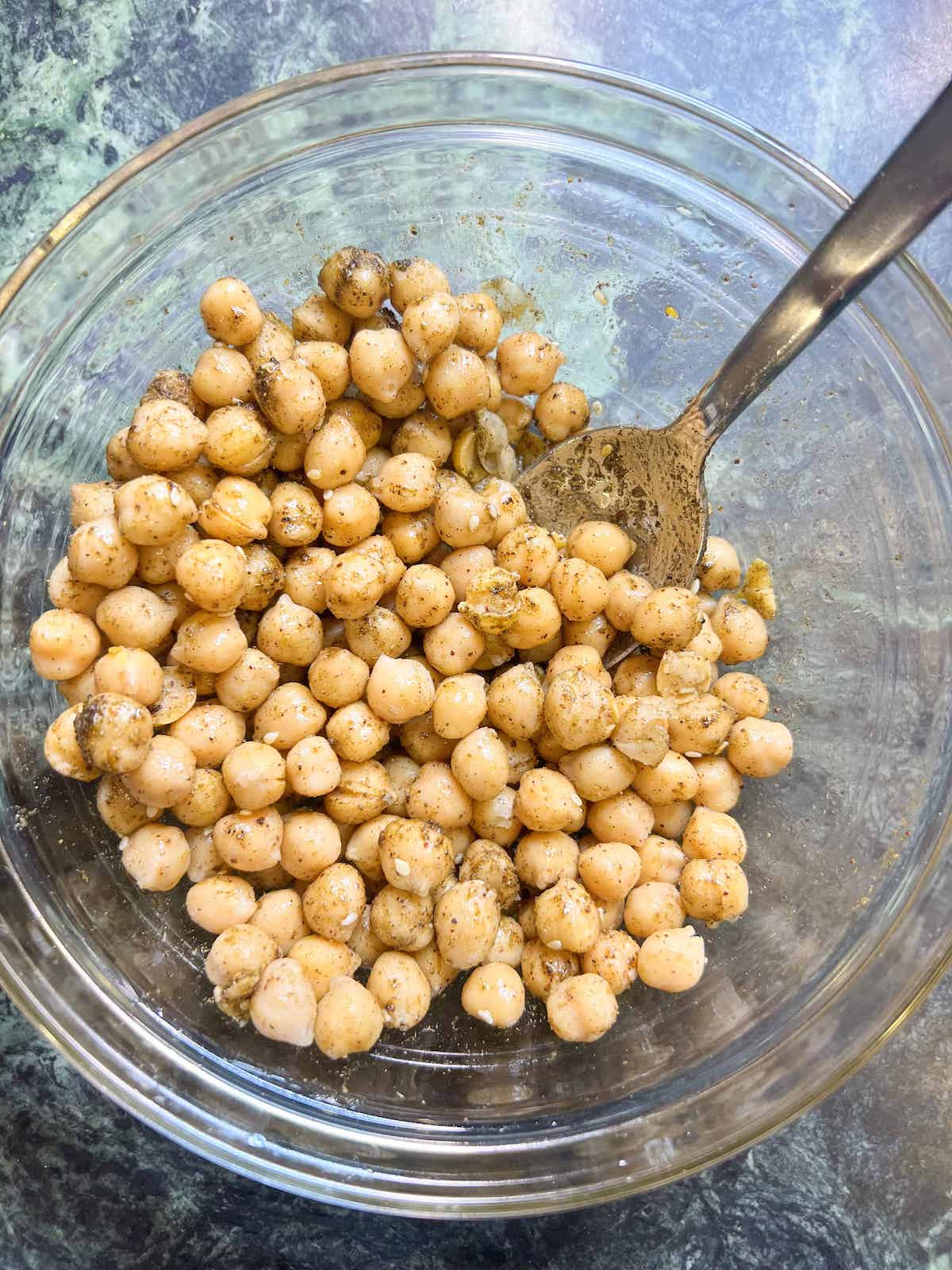 Chickpeas tossed with za'atar spice in a glass bowl with a spoon.