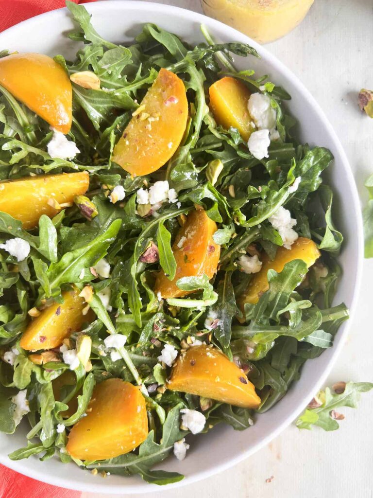 Close up of golden beet and arugula salad with goat cheese and pistachios in a white bowl.