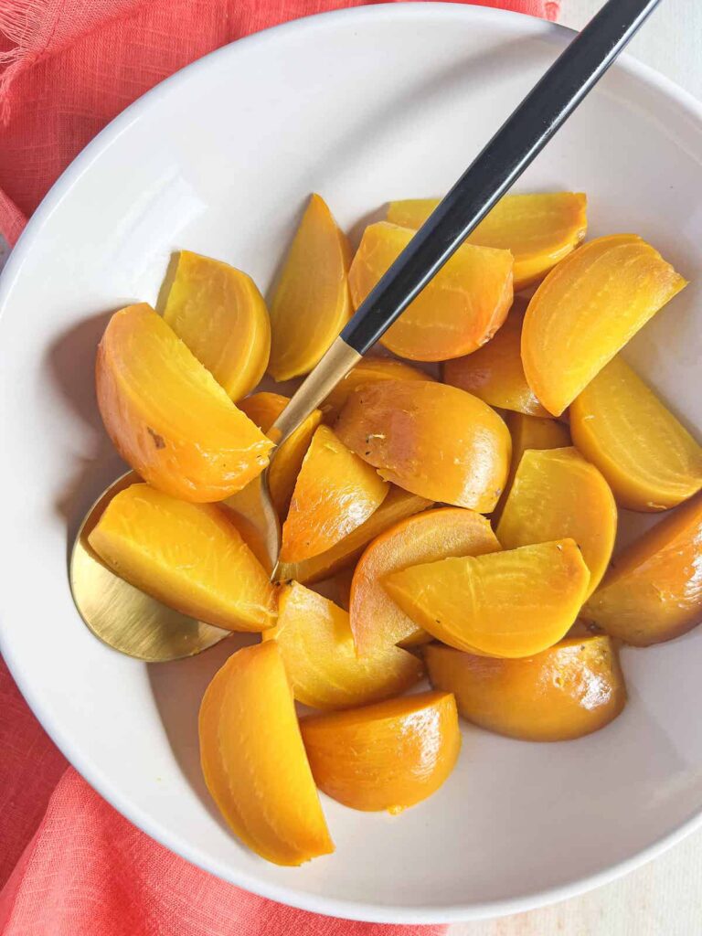 Sliced golden beets in a white bowl with a gold spoon.