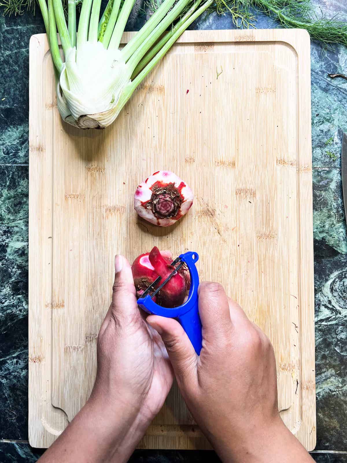 Brown hands peeling Chioggia beets with a blue vegetable peeler.