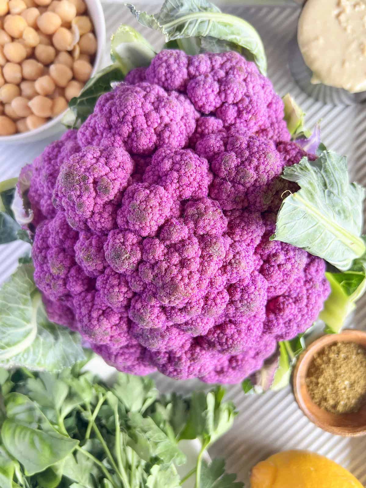 Close up of whole head of purple cauliflower with recipe ingredients in the background.