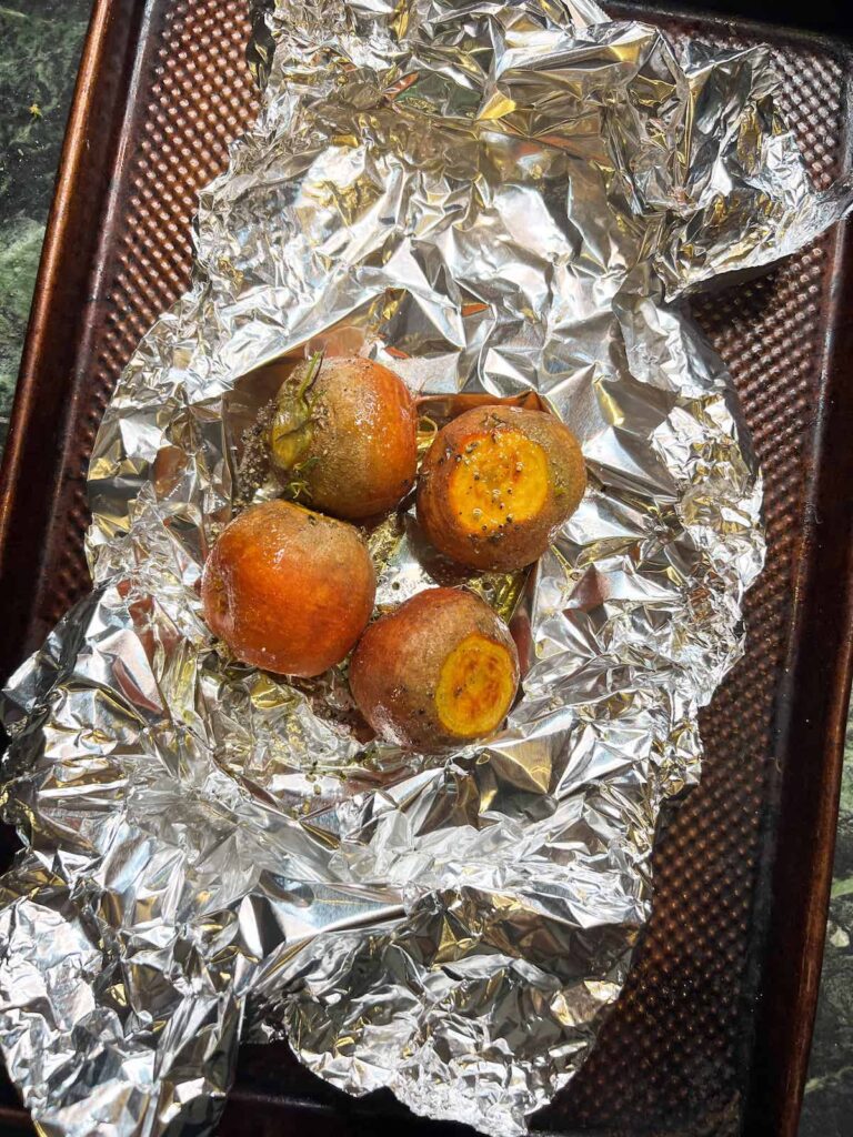 Raw beets with greens removed on a sheet of foil on a baking tray.