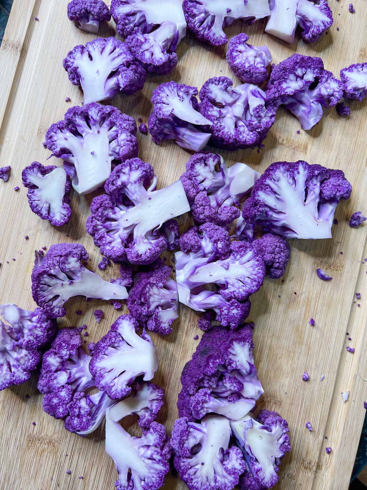Slices of purple cauliflower florets on a wood cutting board.