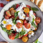 Grey bowl of halved cherry tomatoes, torn burrata and basil leaves.