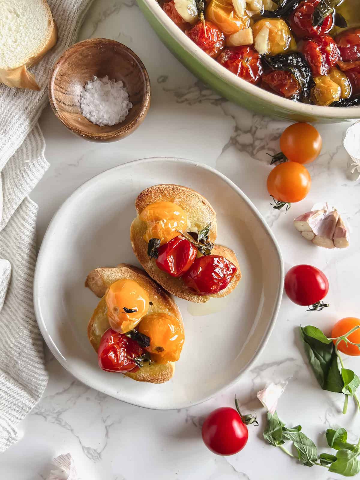 Small plate with two pieces of french bread topped with cherry tomato and garlic confit.