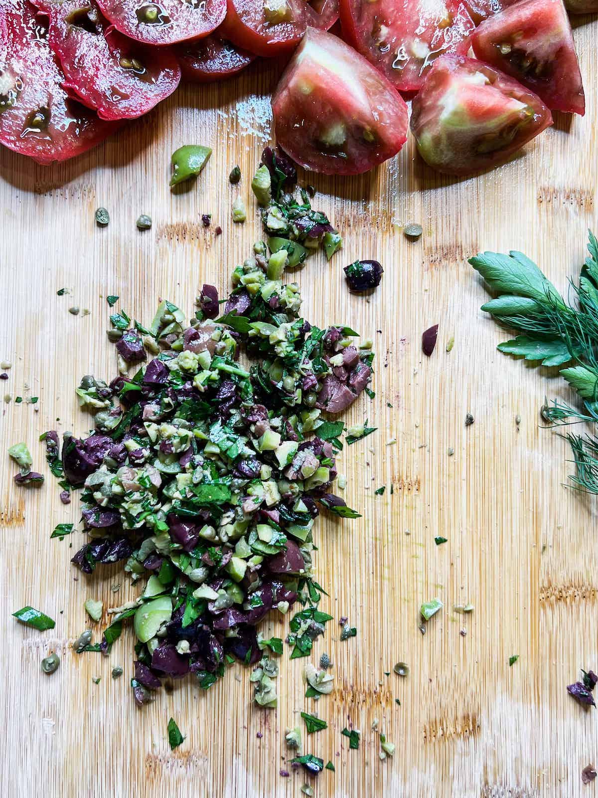 Chopped olives, capers and parsley on a wood cutting board.