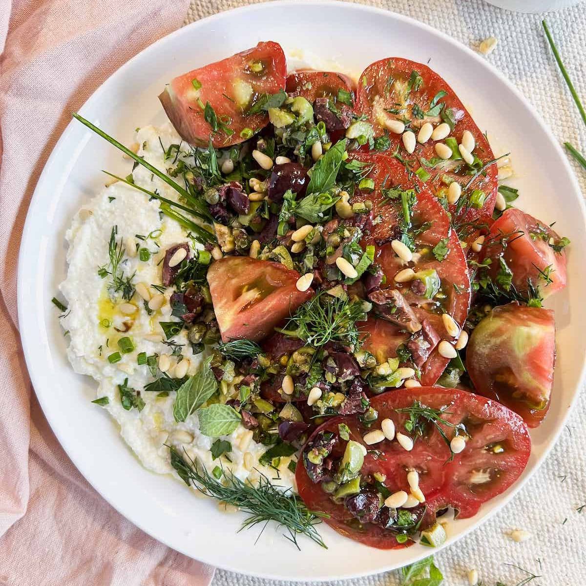 Heirloom tomato salad and whipped ricotta on a white plate.