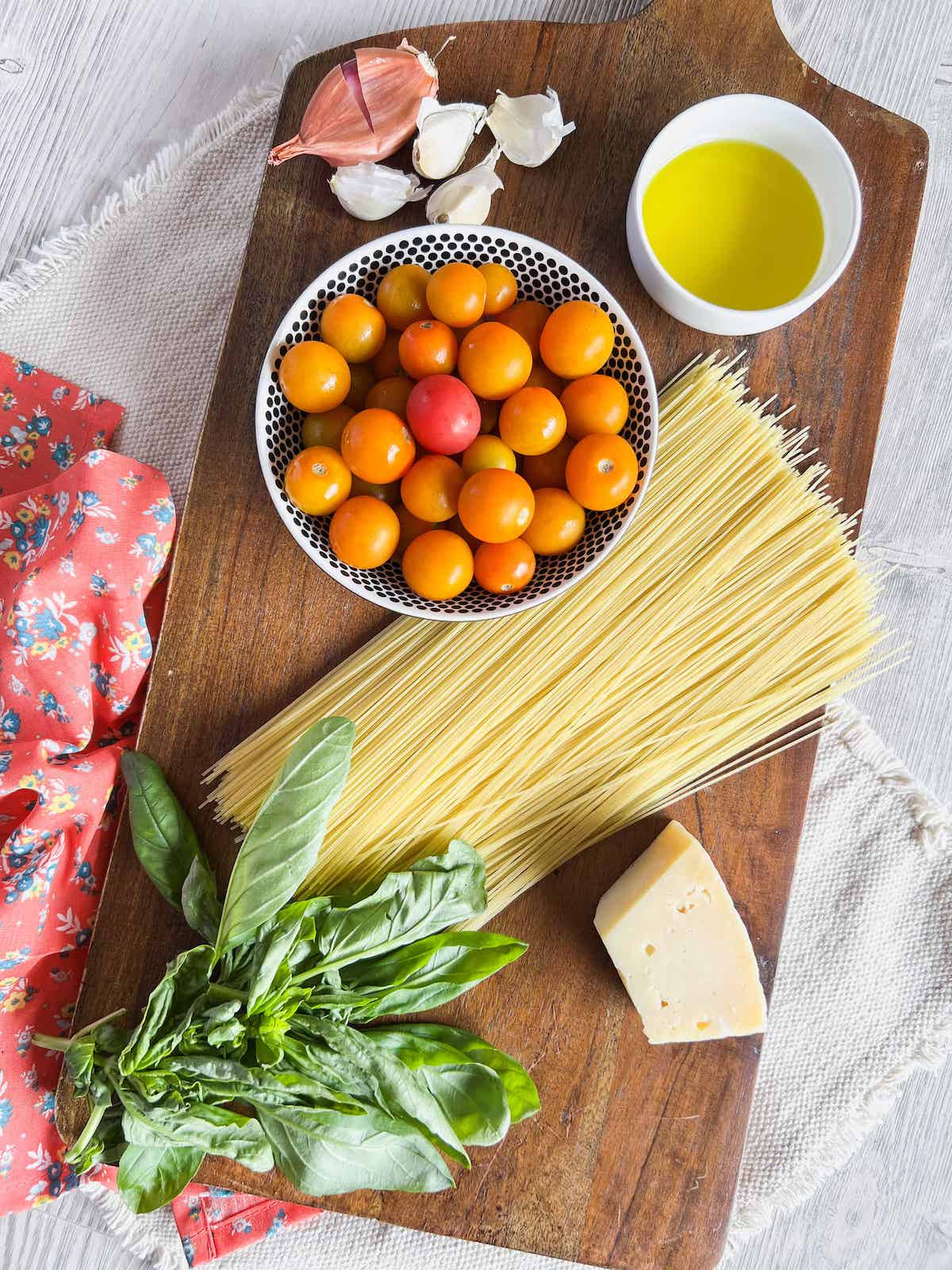 Ingredients for sungold tomato pasta on a wood board with a pink floral napkin.