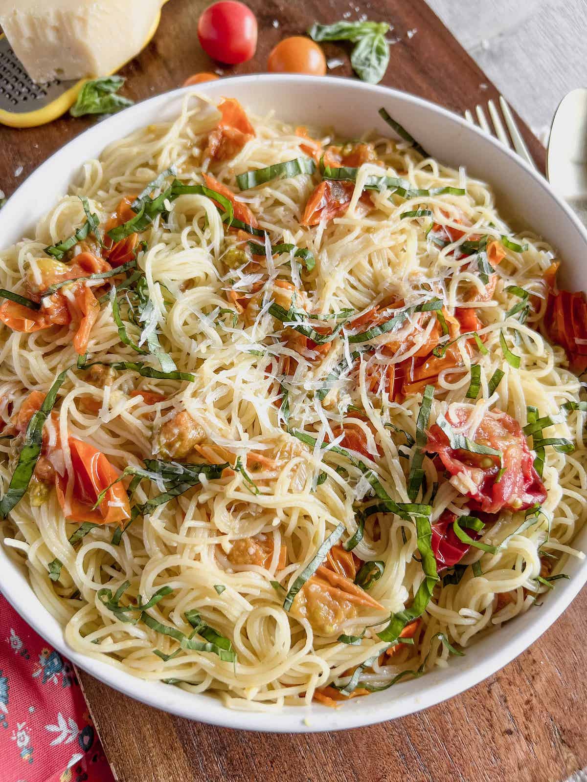 Big white bowl of sungold tomato pasta on a wood board with a floral napkin.