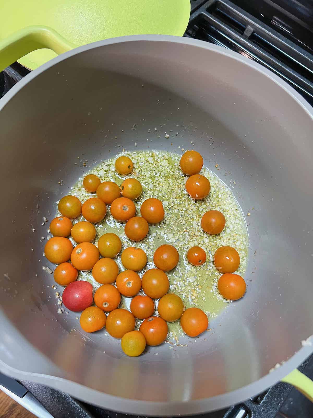 Pot with olive oil, garlic, shallots and whole sungold cherry tomatoes.
