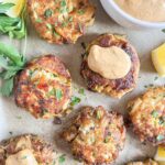 Crab cakes, garnished with parsley, on parchment paper with a dollop of remoulade sauce on one.