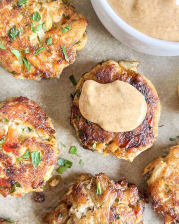 Crab cakes topped with remoulade sauce on brown parchment paper.