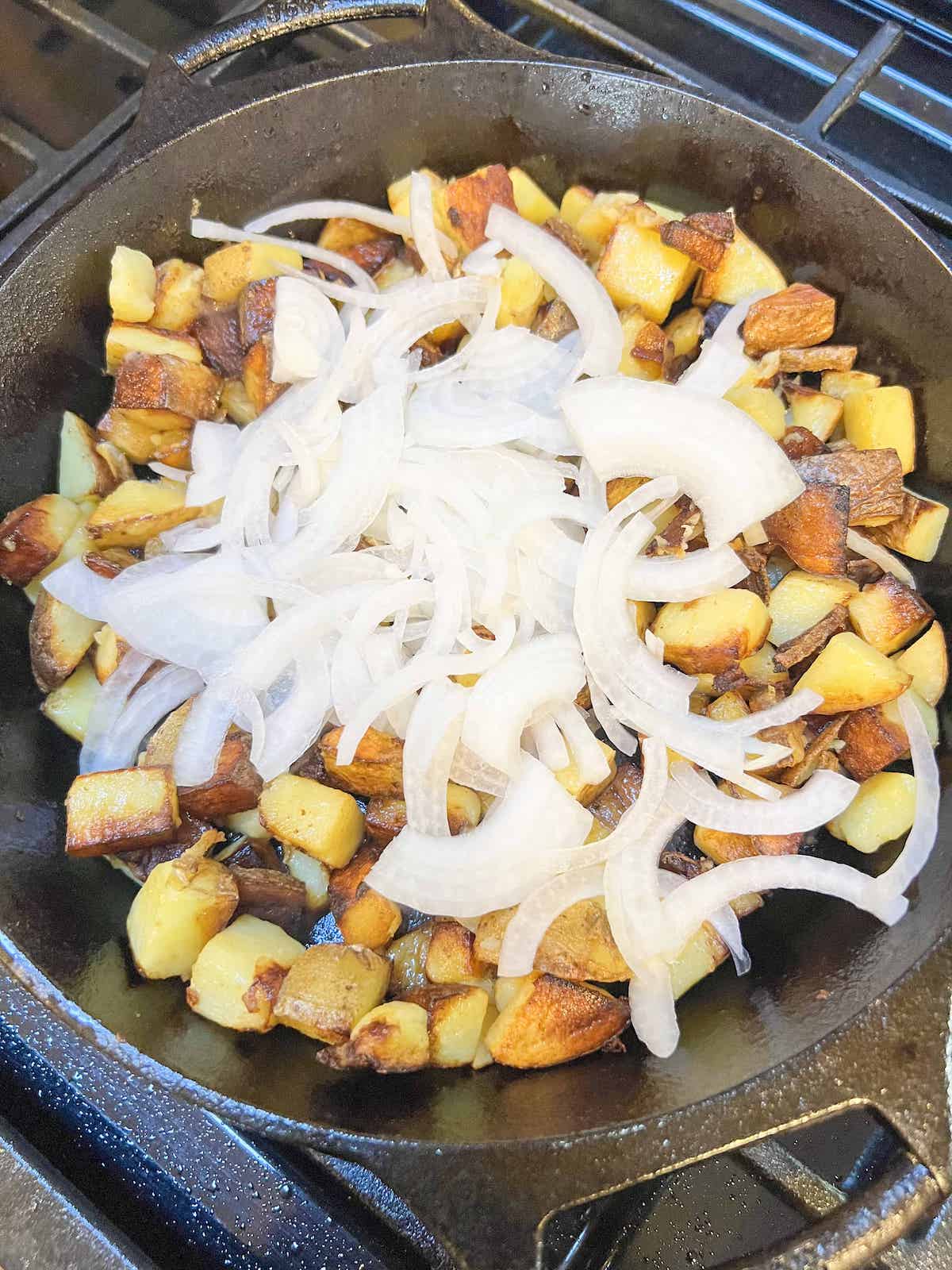 Golden brown cubed potatoes with thinly sliced white onion on top in a cast iron skillet.