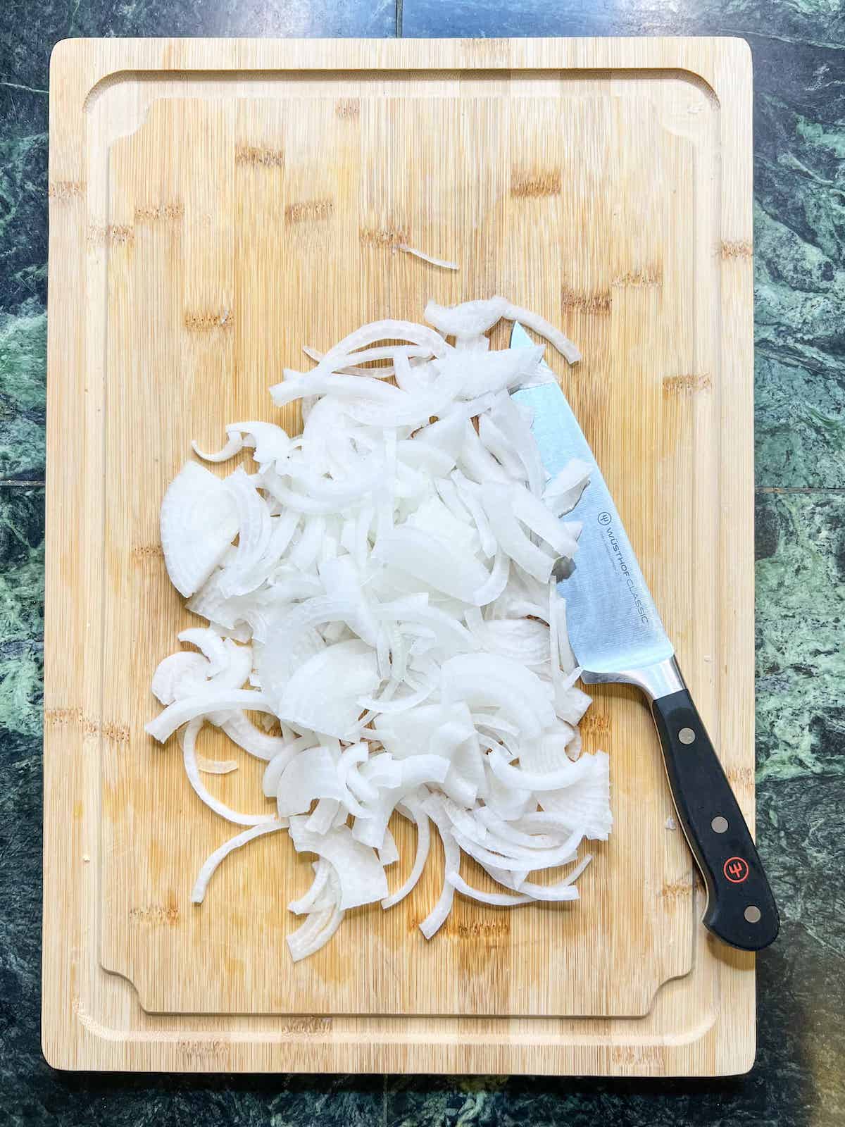 Thinly sliced white onion on a wood cutting board with a chef's knife.