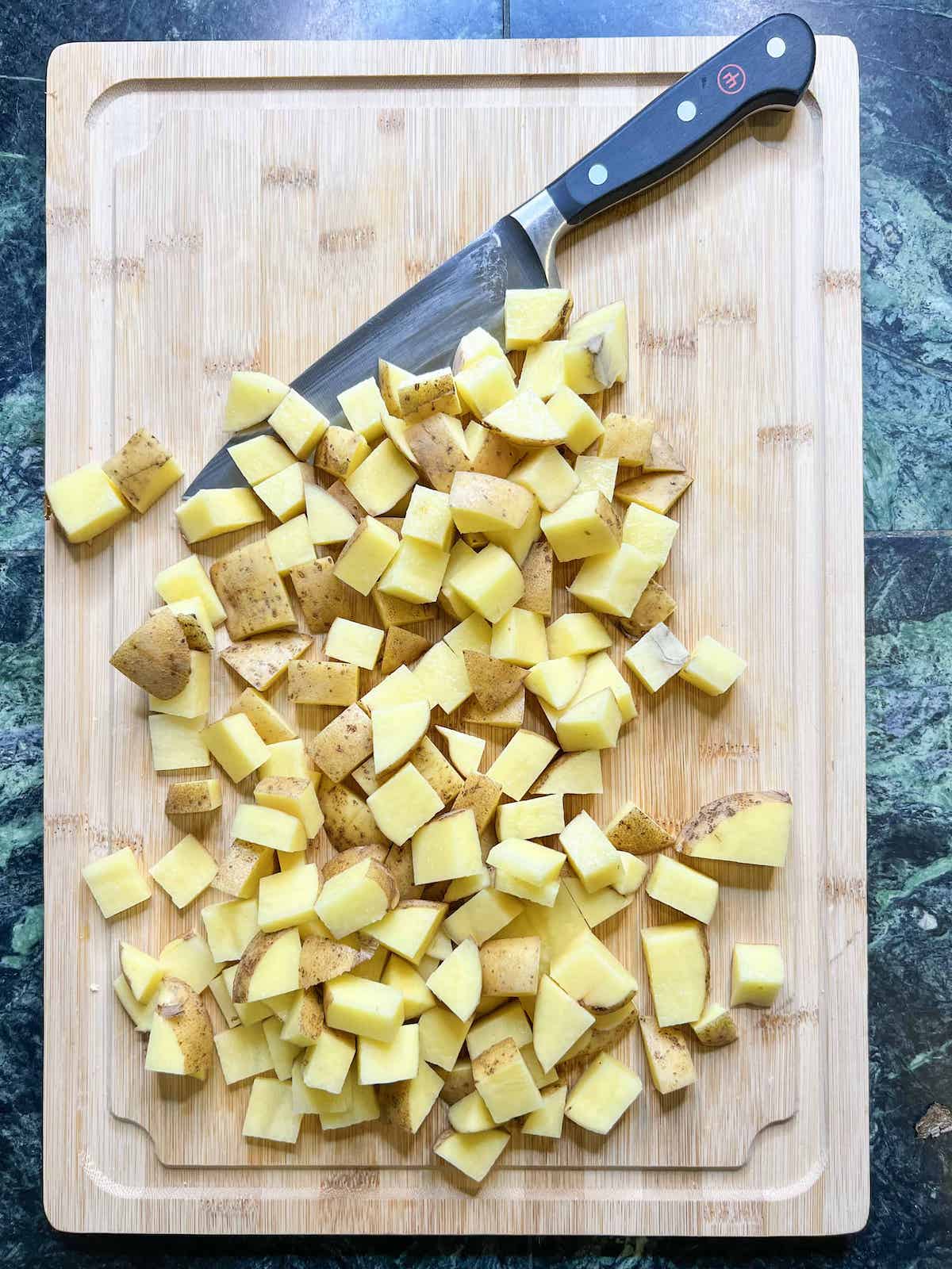 Cubed Yukon gold potatoes on a wood cutting board with a chef's knife.