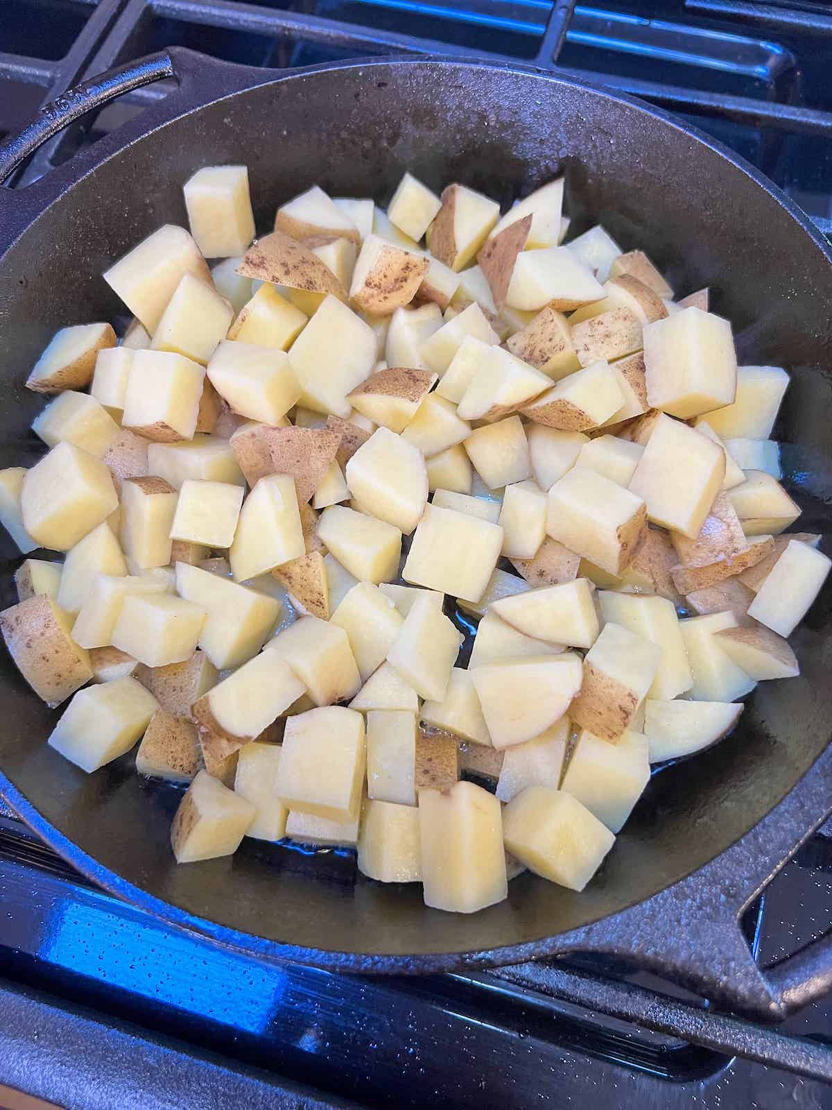 Raw, cubed Yukon gold potatoes cooking in a cast iron skillet.
