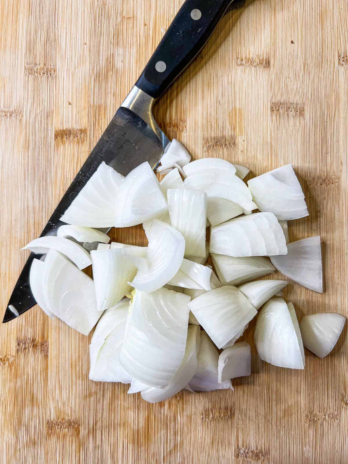 Onion cut into chunks on a wood cutting board with a knife.