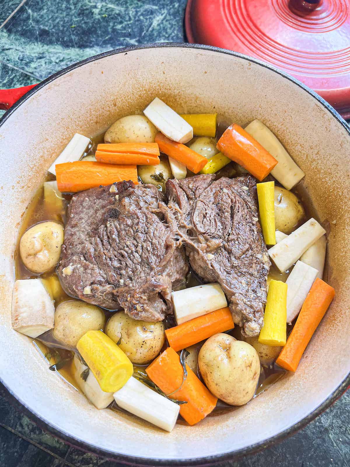 Partially cooked chuck roast with fresh veggies in a dutch oven.