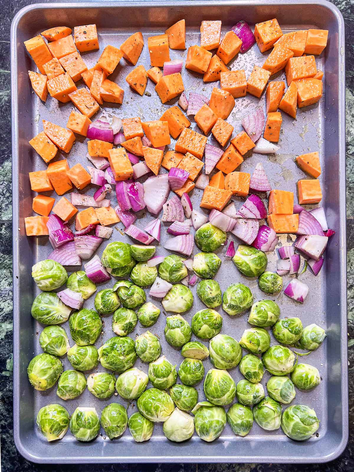 Sweet potatoes, red onion and halved brussels sprouts on a sheet pan.