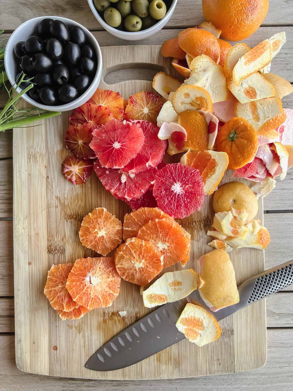 Sliced rounds of mixed citrus fruit on a wood cutting board with a knife.