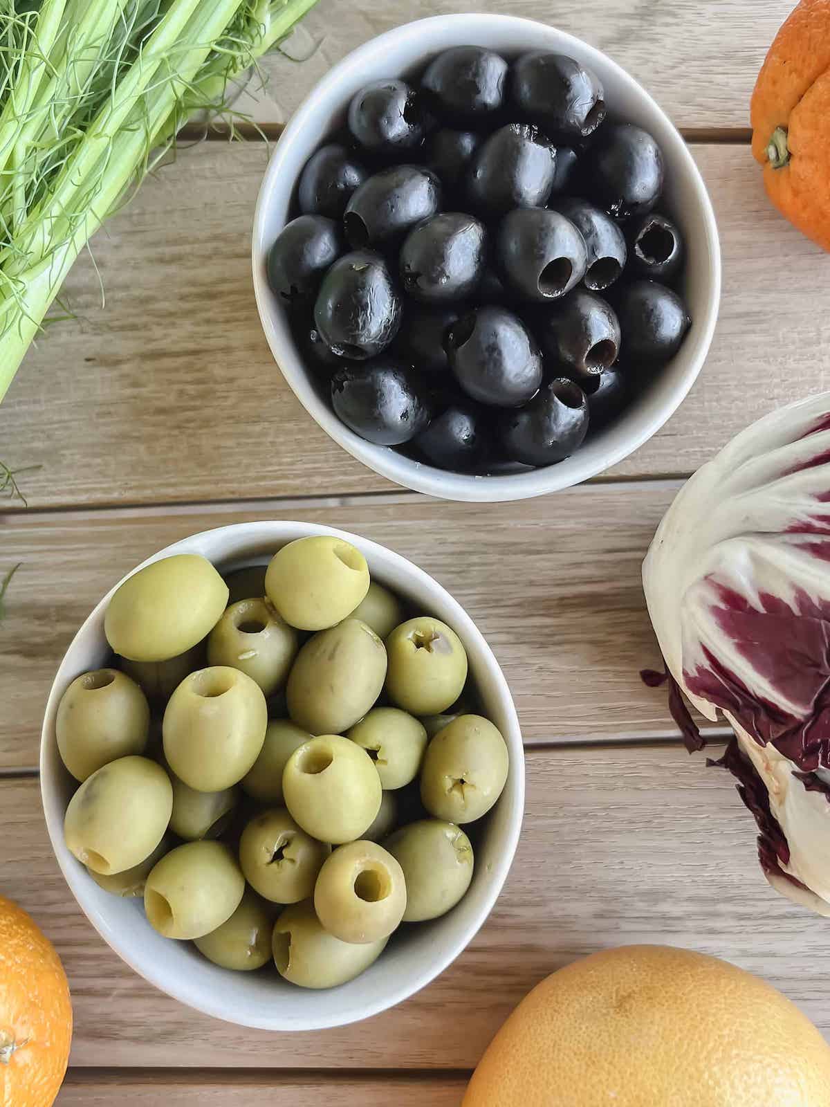 White bowls of black and green olives surrounded with radicchio, citrus and fennel.