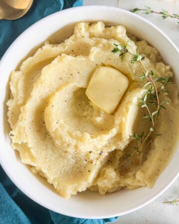 Mashed potato squash in a white bowl with a pat of butter and a sprig of fresh thyme.