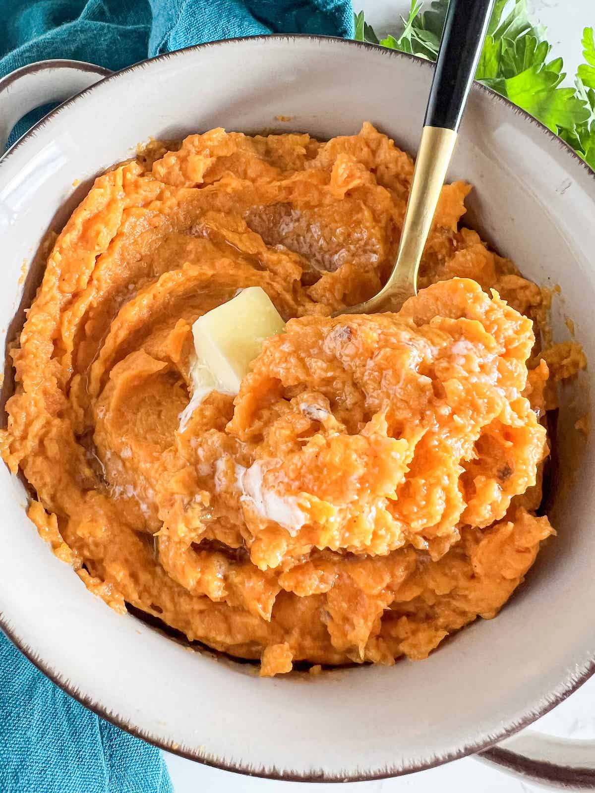Close up of mashed sweet potatoes topped with a pat of butter and gold spoon taking a scoop.
