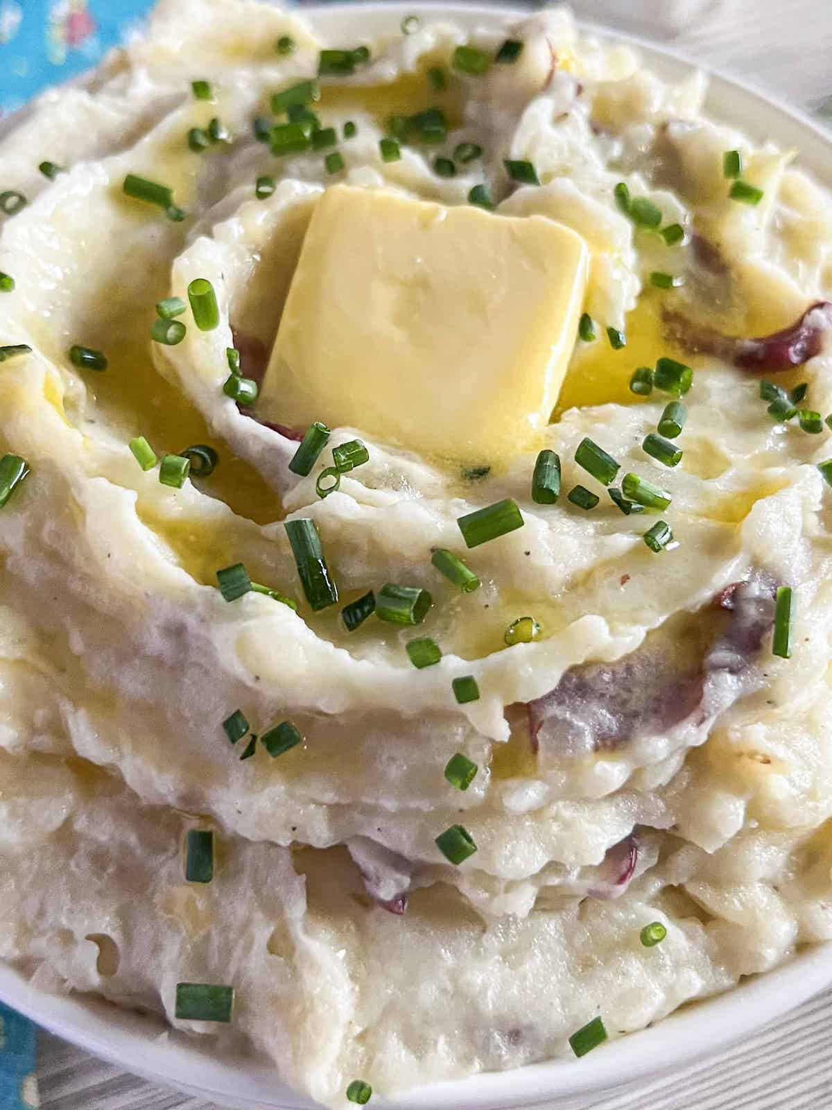 Close up of roasted garlic red skin mashed potatoes topped with chives and a pat of butter.