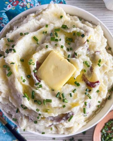 Bowl of roasted garlic redskin mashed potatoes topped with chives and a pat of butter.