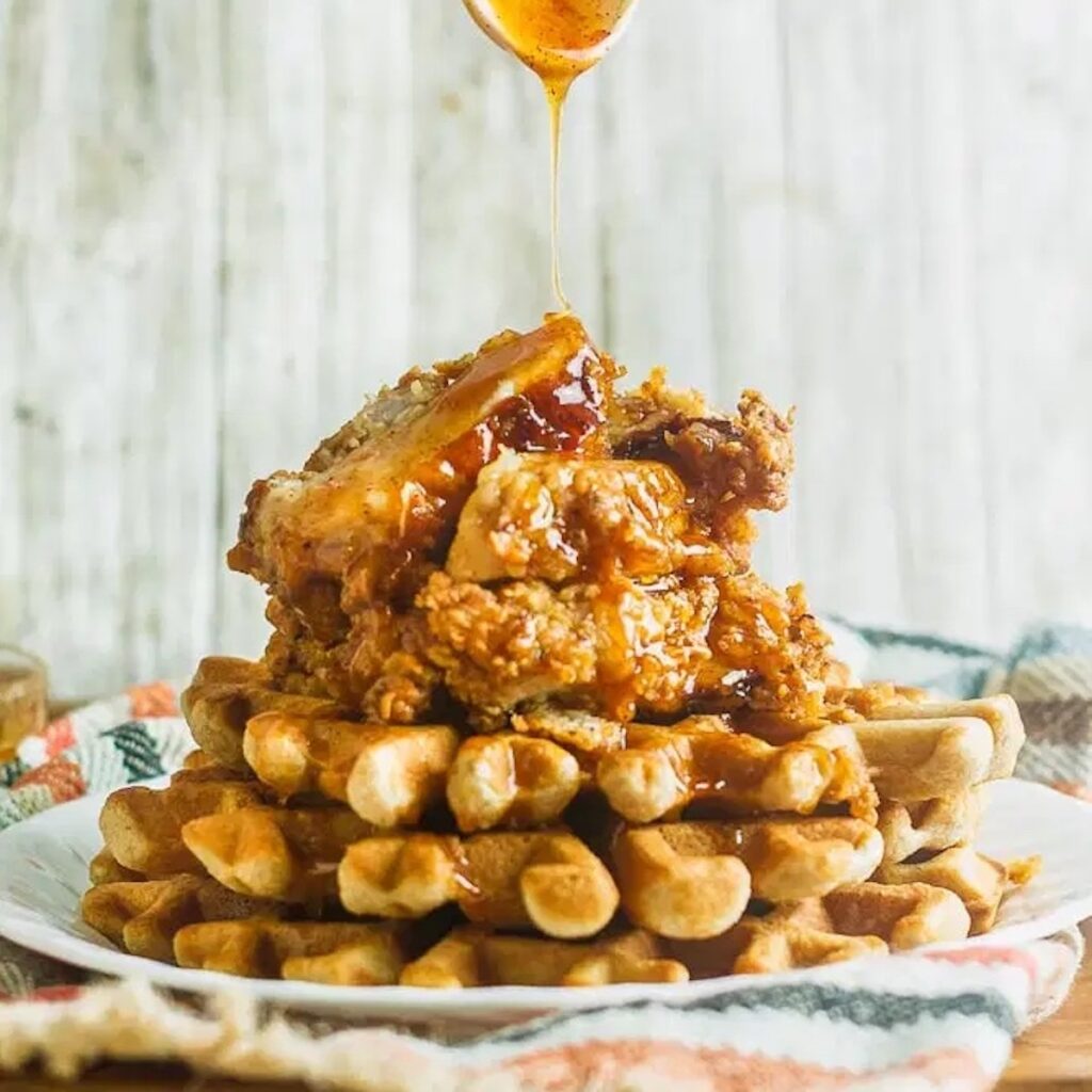 Stack of waffles topped with fried chicken and spoon drizzling honey.