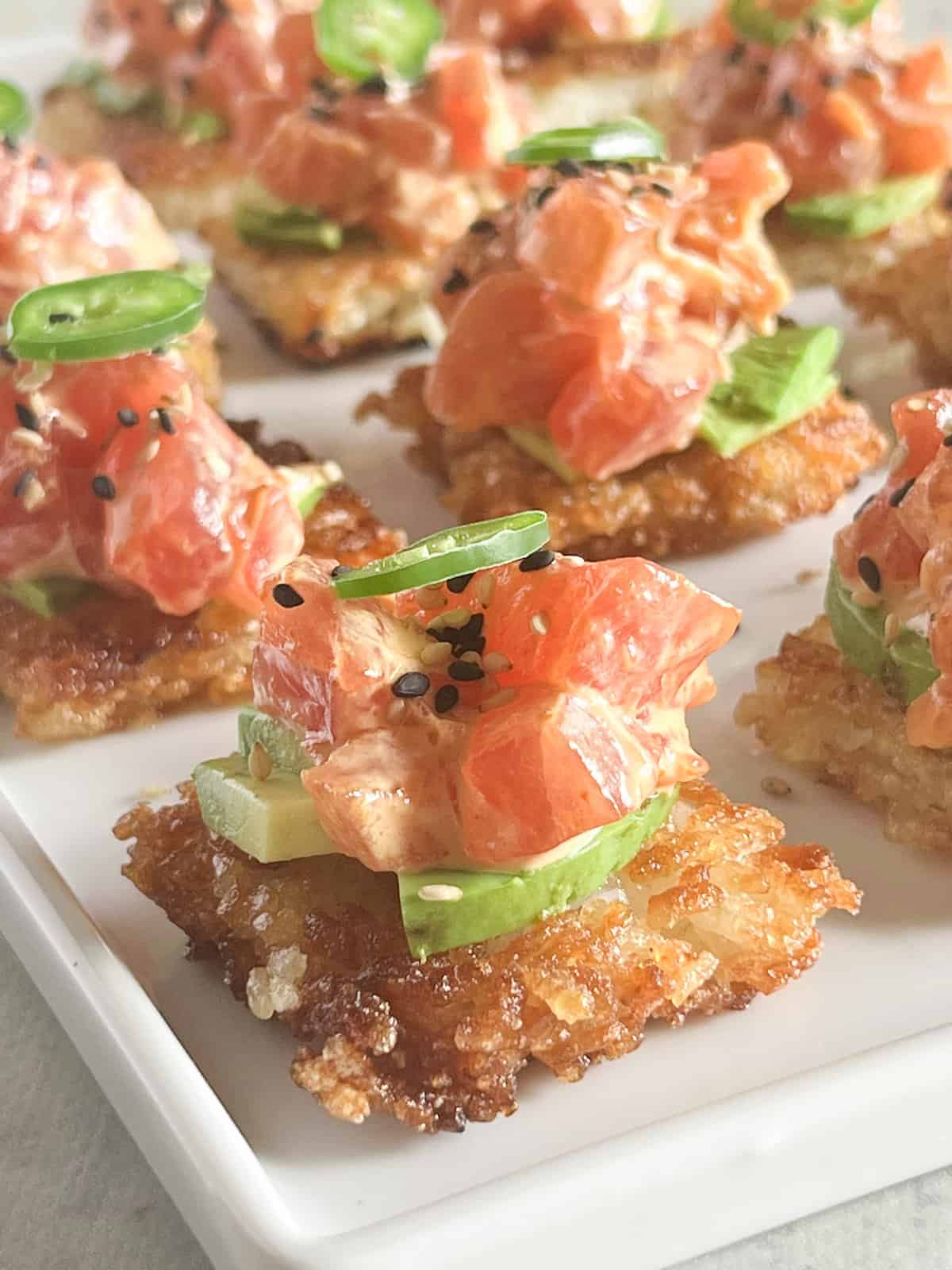 Close up of platter of crispy rice bites topped with avocado, spicy tuna, sesame seeds and thinly sliced Serrano pepper.