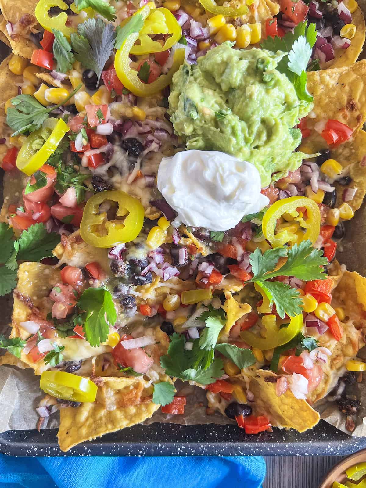 Close up of nachos loaded with cheese, black beans, corn, red onion, peppers, salsa, guacamole and sour cream.