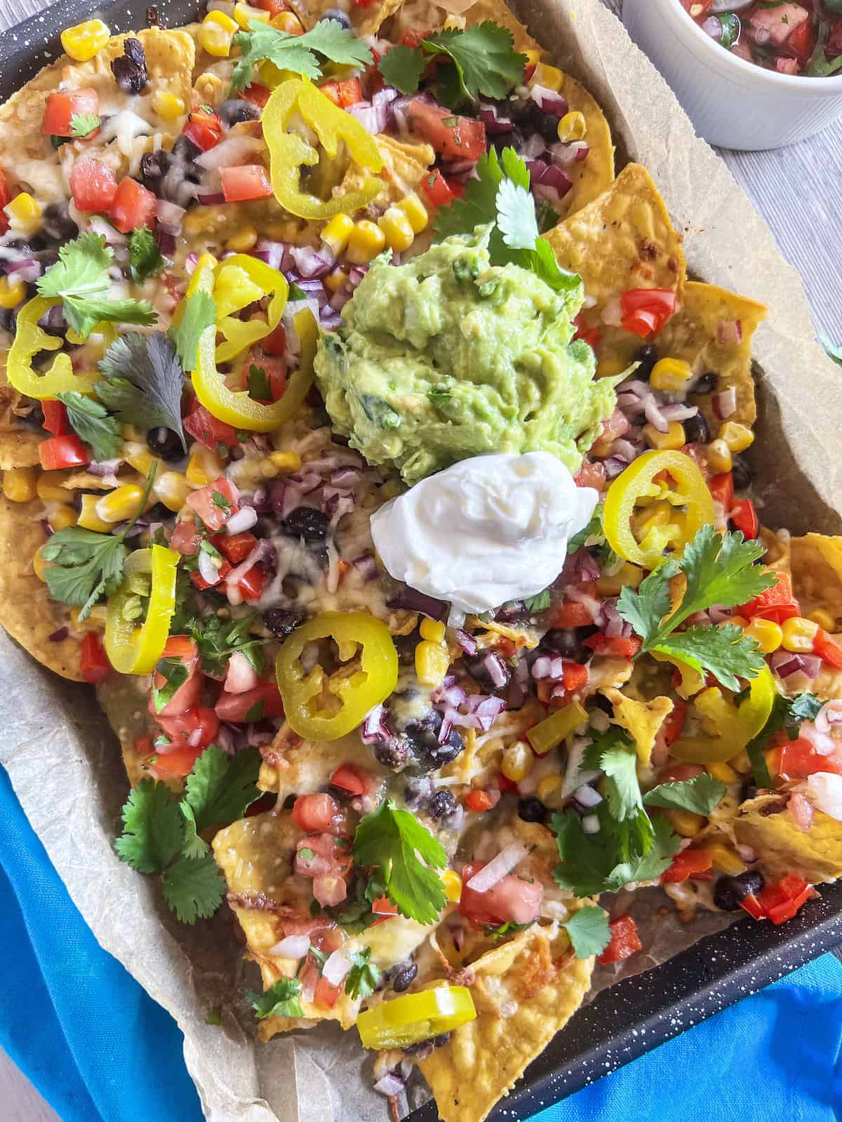 Loaded veggie nachos on a sheet pan with a dollop of guacamole and sour cream.