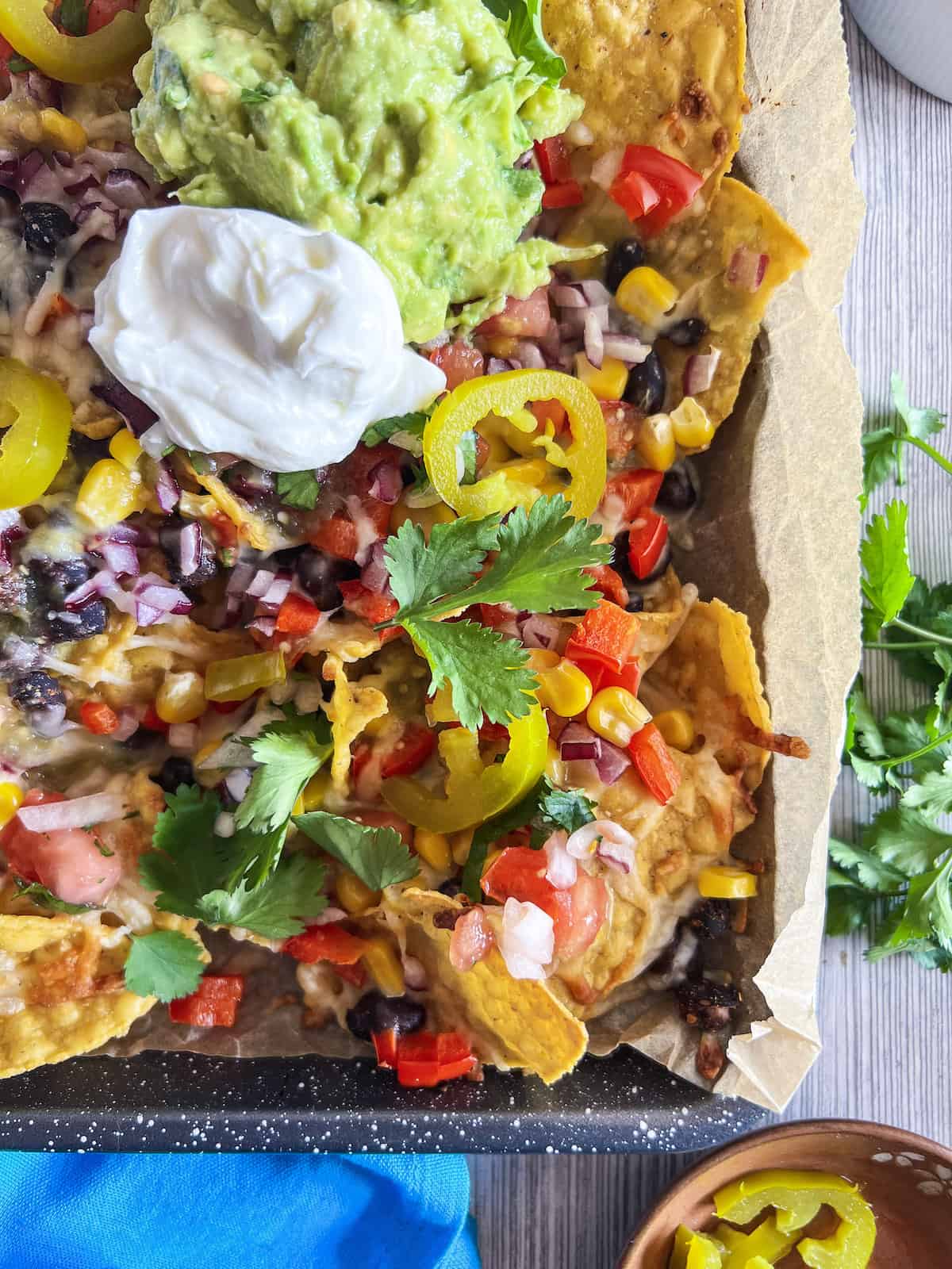 Close up of the corner of a sheet pan with loaded veggie nachos topped with sour cream and guacamole.