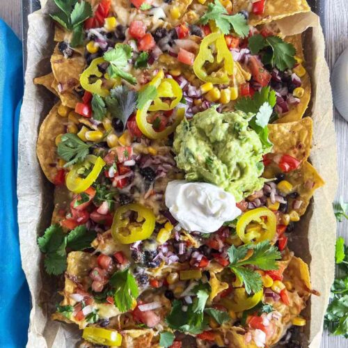 Loaded sheet pan veggie nachos with a dollop of guacamole and sour cream on top.