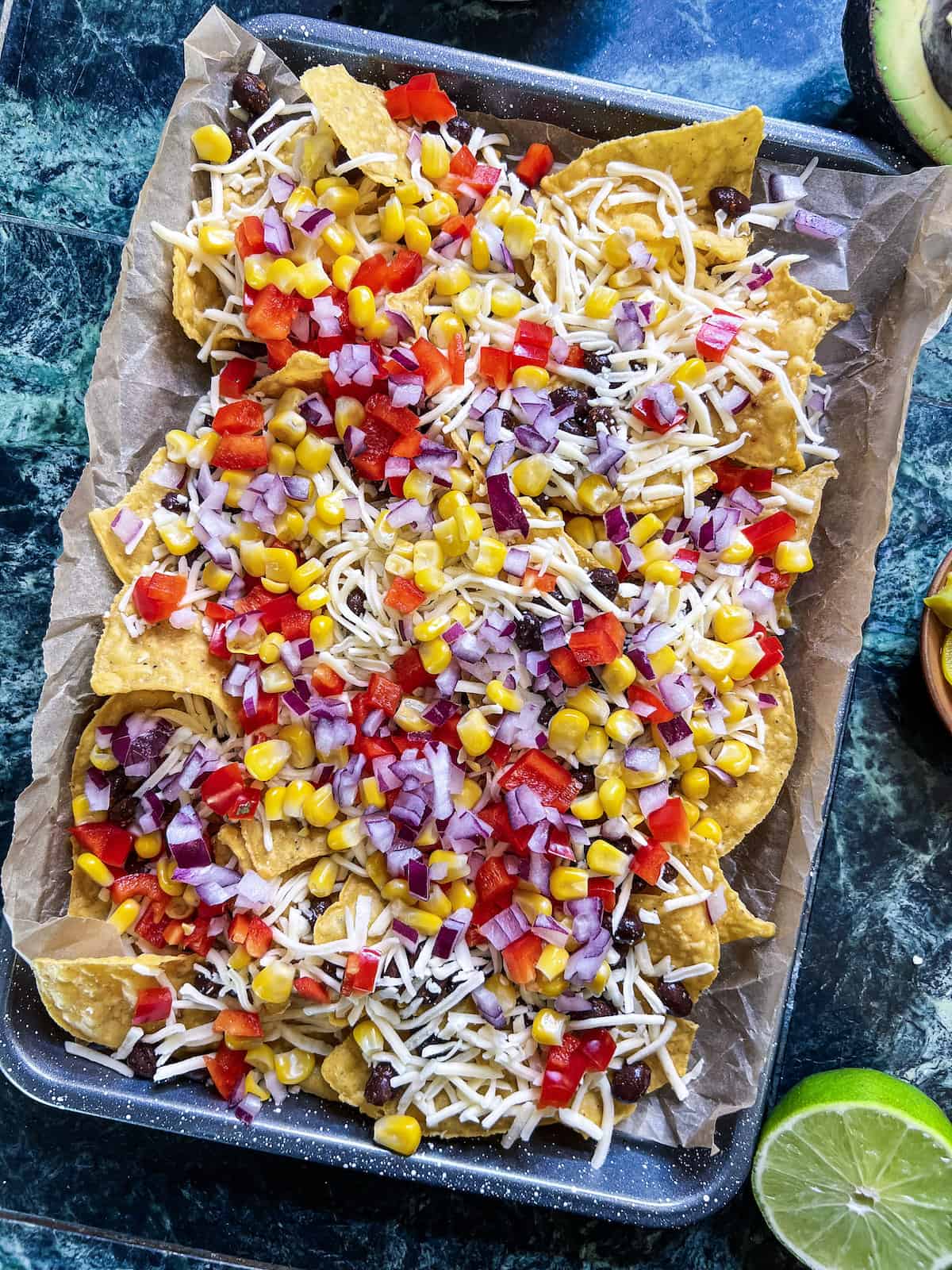 Sheet pan with tortilla chips layered with cheese, beans and finely diced veggies.
