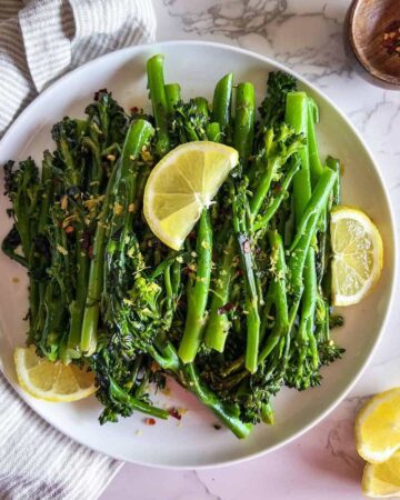 Sauteed broccolini garnished with lemon zest, red pepper flakes and lemon slices on a white plate.