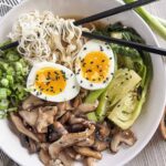 Large white bowl of mushroom and bok choy ramen noodle soup with chopsticks.