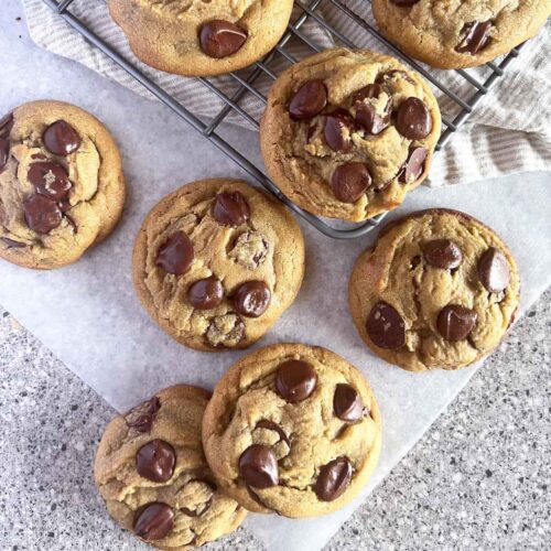 Giant chocolate chip cookies on a wire rack and parchment paper.