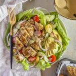 Crispy chicken tender salad on a white plate with a gold fork.