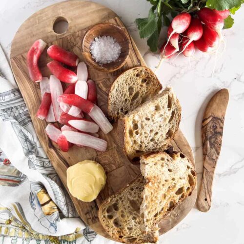 Sliced radishes, butter, salt and toast on a wood board.