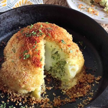 Whole breaded baked cauliflower in a cast iron skillet with a slice cut out.
