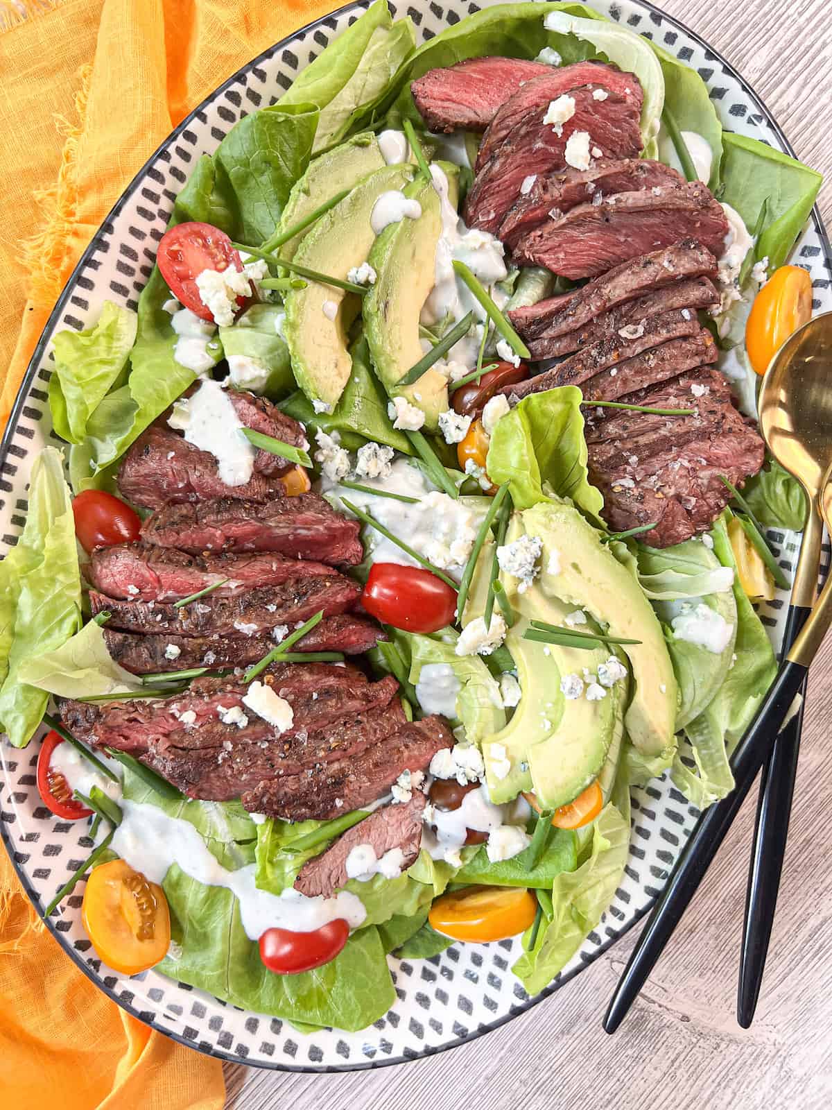 Oval platter of grilled steak salad with a yellow napkin.