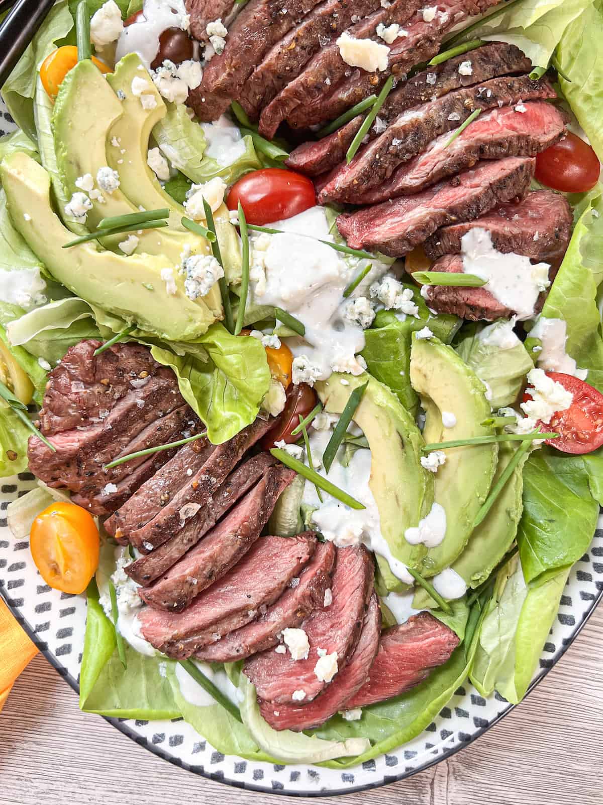Close up of steak salad drizzled with blue cheese dressing on an oval platter.