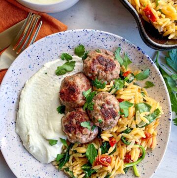 Greek meatballs on a speckled plate with whipped feta and orzo.