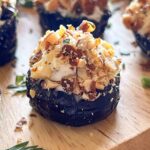 Close up of goat cheese stuffed prune rolled in chopped almonds on a wood board.