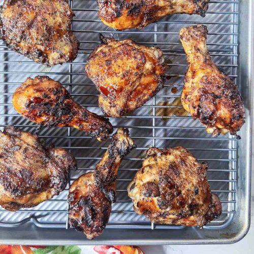 BBQ grilled chicken thighs and drumsticks on a wire rack with a small bowl of barbecue sauce.